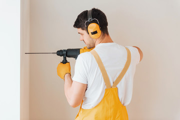 Handyman in yellow uniform works indoors by using hammer drill. House renovation conception