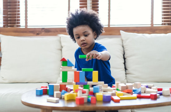 Happy African American cute little child boy play with wooden blocks construction on the table at home. Learning creative concept