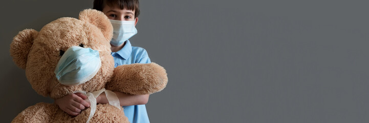 Banner 3:1. COVID-19 quarantine. Boy and teddy bear wearing protective mask on gray background. Selective focus. Flu, illness, pandemic concept
