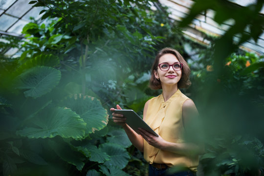 Young woman with tablet standing in botanical garden. Copy space.