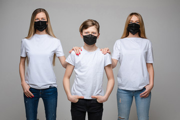 Two woman and teenager boy wearing medical protective mask posing together isolated. Group of illness people in safety bacterial respirator medium shot at white studio background