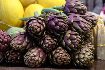 Fototapeta premium Fresh ripe red purple organic globe artichokes displayed for sale at a street food market, side view of healthy vegan food photogrpahed with soft focus