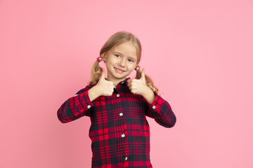 Showing thumbs up. Caucasian little girl's portrait on pink studio background. Beautiful female model with blonde hair. Concept of human emotions, facial expression, sales, ad, youth, childhood.