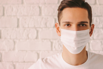 Portrait of tired young man in white medical mask on face for personal protection during coronavirus COVID-19 pandemic. Exhausted confident doctor wearing protective face mask. Prevention of nCov-19