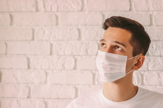 Portrait Exhausted Young Man Wearing Protective Mask On Face And Looking Up On Copy Space. Tired Thoughtful Doctor In White Medical Face Mask. Personal Protection Measures Against Coronavirus COVID-19