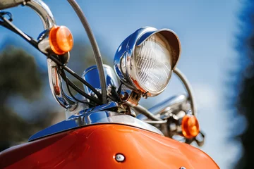 Fotobehang Closeup chroom detail en koplamp van oranje retro vintage scooter onder blauwe lucht en zon op de onscherpe achtergrond. © B@rmaley