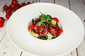 Vegetable salad with meat and barbecue sauce served on a large round white plate. Restaurant dish on a wooden background.