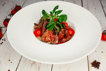 Vegetable salad with meat and barbecue sauce served on a large round white plate. Restaurant dish on a wooden background.