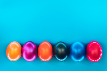 Glossy colorful eggs in neon trendy colors with creative backlight on blue background. Easter concept. Flat lay style.
