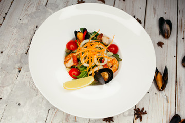 Salad of vegetables and fried shrimp. The table is decorated with freshly opened mussels and star anise.