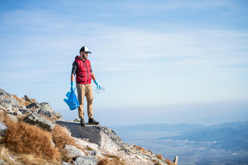 Man hiker picking up litter in nature in mountains, plogging concept.