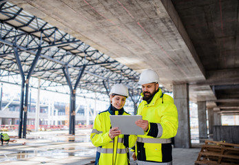 Engineers standing outdoors on construction site, using tablet.