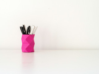 Pink pen holder made of paper with geometric low poly technique on a white table