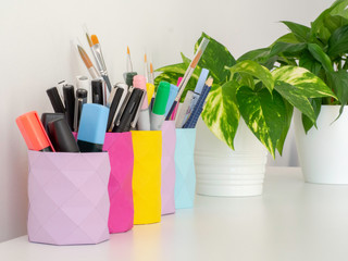 Pen and pencil holders made of paper with geometric forms coloring a white table