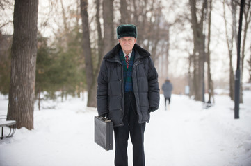 An old smiling man with case standing outdoors in winter park