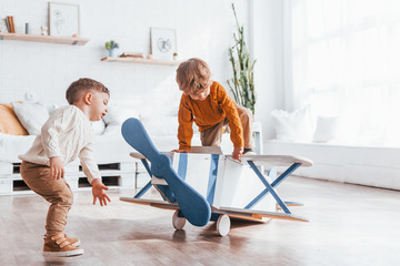Two little boys in retro pilot uniform having fun with toy plane indoors © standret