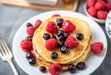 Sweet homemade pancakes with raspberries and blueberries on white plate.