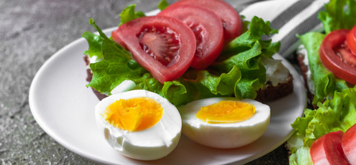Eggs boiled cut and healthy sandwich from ray bread with cream cheese, tomatoes and lettuce for breakfast. Banner