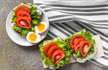 Healthy food for snack or lunch. Boiled cut eggs and sandwiches. Rye bread with cream cheese, tomatoes and lettuce on cement background and linen towel. Flat lay design