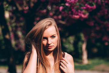 Closeup portrait of a lovely girl in a park with blooming Japanese sakura trees. Romantic young blonde in a dress posing on a background of spring flowering trees. Cherry blossoms.