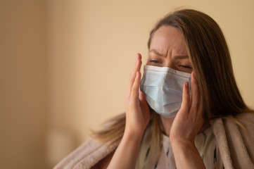 Girl in a mask and temperature with a coronavirus. Symptoms of temperature, covered with a blanket, in the room