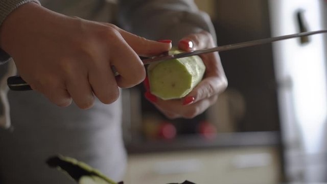 Girl in home clothes kitchen preparing food. Cleans eggplant peel large uncomfortable blunt knife which spoils pleasure cooking Tears off pieces cleans unevenly Advertising cleaners kitchen appliances