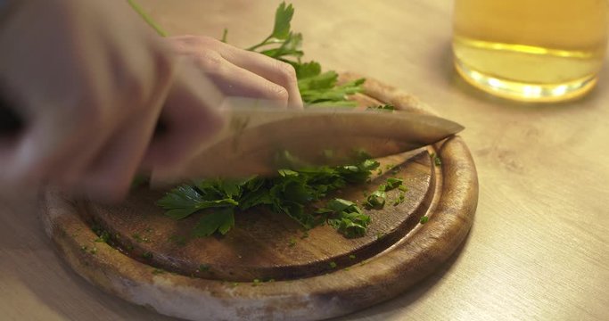 Chopping parsley on chopping board, healthy food. Parsley cutting in kitchen. Woman cutting up parsley for recipe 