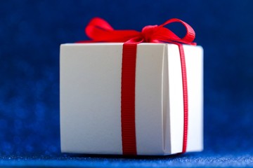 White gift box tied with a red ribbon on a blue background. Gift.