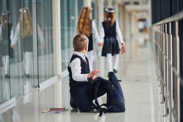 Boy sitting on the floor. School kids in uniform together in corridor