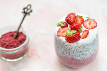 Chia seed pudding with almond milk, yogurt and pitaya dragon fruit powder in a glass. Superfood and vegan food concept. Pink background. Copy space, selective focus.