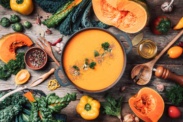 Pumpkin soup with vegetarian cooking ingredients, wooden spoons, kitchen utensils on wooden...