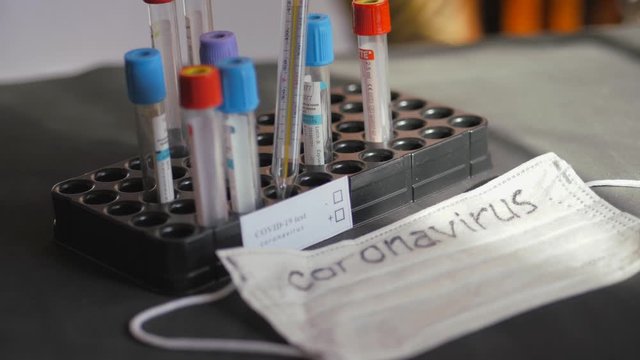 Coronavirus. Medical test tubes are in the organizer. Medical disposable gauze bandages are on the table. A mercury glass thermometer rests on a protective medical mask.