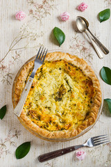 Vertical top view of a delicious quiche surrounded by flowers, leaves and rustic forks and spoons in a fresh, spring setting. Healthy food. Cooking at home.
