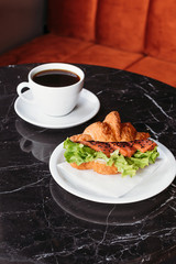 Croissant with salmon and herbs. Breakfast in cafe. Croissant with cup of black coffee.