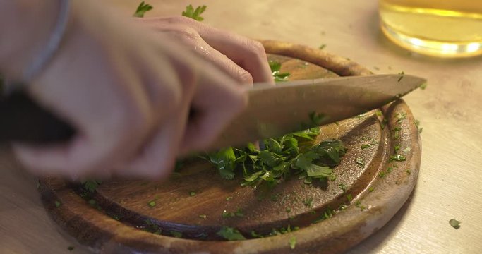 Cutting parsley in small pieces on a wooden chopping board by woman. Cooking healthy. Cutting with knife on wooden surface
