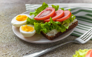 Fototapeta na wymiar Boiled eggs cut in half and sandwich with rye bread, cream cheese, sliced tomatoes and fresh lettuce for healthy breakfast/lunch