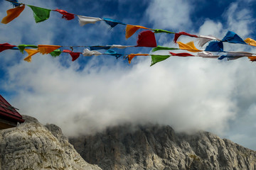 Prayer flags waving with the strong wind in Alpine mountain range at Austrian-Italian border. Sharp rocky Alpine peaks. Serenity and peace. Clouds breaching high mountains. Mantra and peace of mind