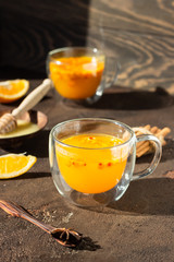 Colorful hot spicy sea buckthorn tea with cinnamon, anise and honey in glass cup on dark brown concrete background, selective focus. Vitamin drink.