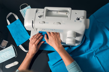 Hands sewing fabric with machine to make homemade surgical masks due to lack of material during covid-19 coronavirus crisis.