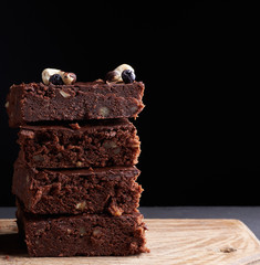 stack of square baked slices of brownie chocolate cake with walnuts on a wooden surface