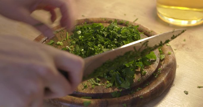 Cutting parsley in small pieces on a wooden chopping board by woman. Cooking healthy