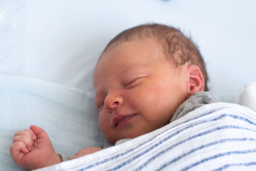 Happy smiling newborn baby boy sleeping in baby bed under striped blanket. Sweet dreams of a cheerful new born.