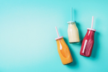 Bottles of orange, white, pink smoothie with straws on blue background. Top view. Flat lay. Copy...