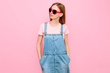 stylish attractive young girl in sunglasses, posing on an isolated pink background
