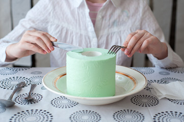 A roll of toilet paper lies on a plate. Girl wants to eat it with a knife and fork.