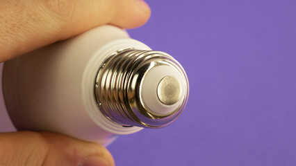 the base of a light bulb in the hands of a person on a purple background