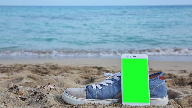 High quality 10bit footage of SmartPhone with green screen on the beach and ocean waves on background. Perfect for screen compositing. Made from 14bit RAW