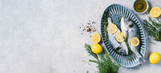 Uncooked dorado or sea bream fish with lemon, herbs, oil, vegetables and spices on concrete background. Top view. Healthy food concept. Copy space. Food pattern