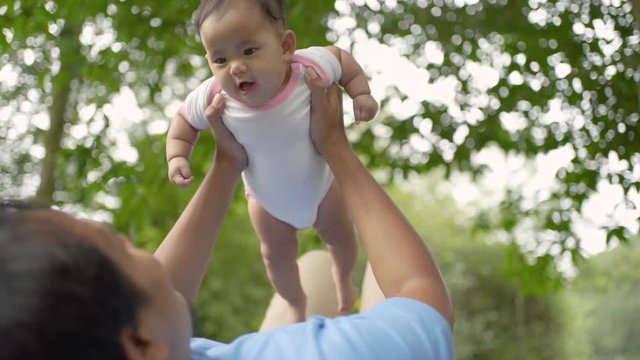 little baby laughs when his father lift him up while lying on the grass