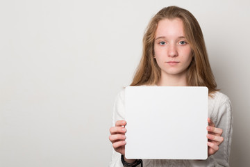 Naklejka premium Positive girl holds a blank poster for text. Schoolgirl with a smile holds a white sheet for text.